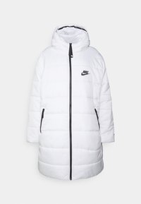 Biała pikowana kurtka puchowa Nike z kapturem, zapinana na zamek z przodu, z dwoma czarnymi bocznymi kieszeniami i czarnym logo na piersi. Teksturowany, pikowany wzór.