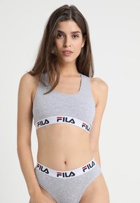 Reggiseno sportivo grigio abbinato a mutandine a vita alta con una fascia bianca che mostra il logo FILA in rosso e nero. Texture del tessuto liscia.