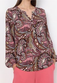Blouse à manches longues avec un motif paisley multicolore dans des tons de rose, noir et or, dotée d'un col en V et de poignets froncés.