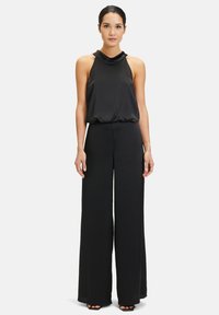 Svart jumpsuit med halterneck-design, flödande ovandel och vida byxor. Slät tygkvalitet med avslappnad passform och minimala detaljer.