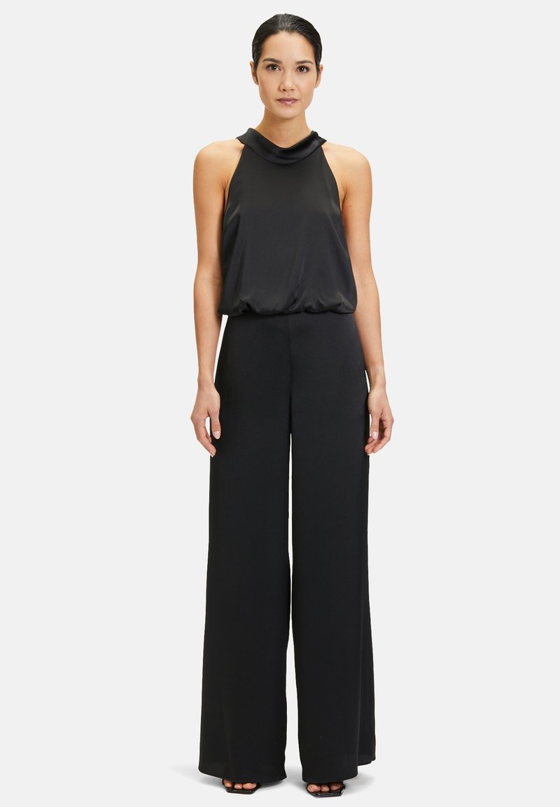 Svart jumpsuit med halterneck-design, flödande ovandel och vida byxor. Slät tygkvalitet med avslappnad passform och minimala detaljer.