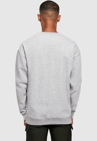 Sudadera gris hecha de una tela suave, con mangas largas, cuello redondo y puños y dobladillo de canalé. Vista trasera mostrada.