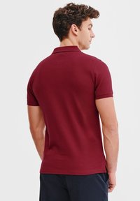 Bordowa koszulka polo z kołnierzykiem, krótkimi rękawami i prostym dołem. Miękka faktura materiału, minimalistyczny design, bez widocznych logo.