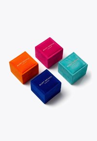 Vier Samtschmuckkästchen in Orange, Pink, Blau und Türkis, jeweils mit goldener Aufschrift "Kurt Geiger London." Quadratische Form mit einer weichen Textur.