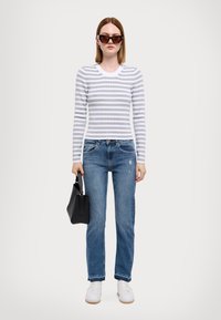 Top a maniche lunghe a righe grigie e bianche, jeans blu, sneaker bianche, borsa nera e occhiali da sole. Vestibilità casual con dettagli minimi.