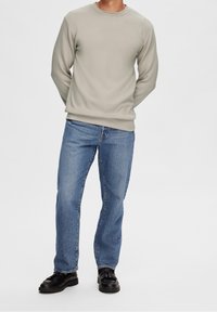 Sudadera gris claro de manga larga, con cuello redondo, combinada con jeans rectos azules y zapatos negros. Diseño simple, sin patrones visibles.