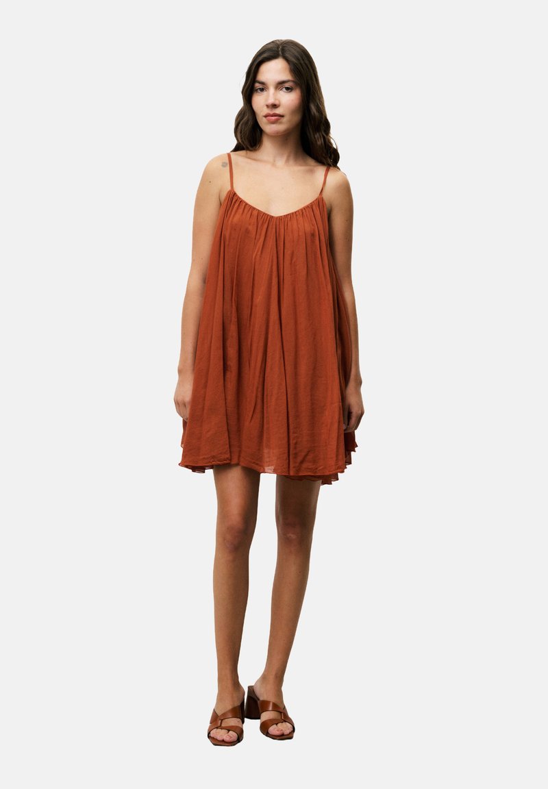 Rostfarbiges ärmelloses Kleid mit gerafftem Oberteil, fließender Silhouette und Oberschenkel-langer Länge. Kombiniert mit braunen Absatzsandalen.