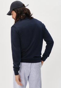 Marineblaues Sweatshirt mit langen Ärmeln, gerippten Bündchen und Saum. Kombiniert mit leicht gestreiften Hosen. Glatte Textur und lässige Passform.