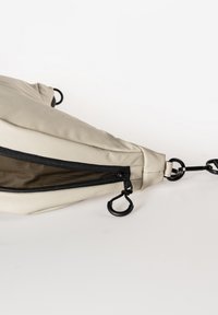 Beige Stoffbeutel in dreieckiger Form, mit einem schwarzen Reißverschluss, schwarzen Hardware-Akzenten und einem strukturierten Innenraum.