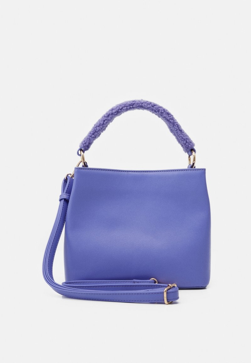 Petit sac à main violet compact avec une poignée supérieure douce texturée et une bandoulière réglable plus longue, sur un fond uni clair.