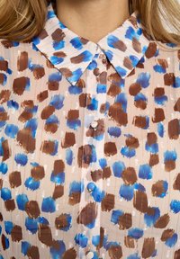 Doorschijnende blouse met een bruin-blauw gevlekt patroon, voorzien van een spitse kraag, knopen en delicate verticale strepen. Zachte textuur.