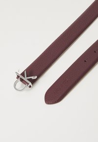 Cinturino in pelle bordeaux con finitura testurizzata, dotato di una fibbia circolare in argento e un accent decorativo argenteo. Estremità a taglio dritto con fori.