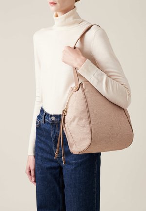 Borsa a tracolla beige con una forma arrotondata e una singola tracolla, caratterizzata da dettagli con zip e hardware dorato, abbinata a jeans blu.