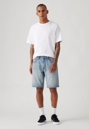 White cotton t-shirt, light blue denim shorts, and black sneakers with white accents. Styled with crew socks, showcasing a casual look.