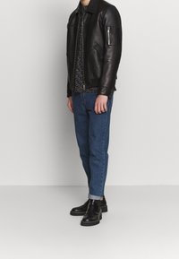 Sort læderjakke med en lynlås lomme, parret med blå denim jeans og sorte ankelstøvler. Jakken har et struktureret design.
