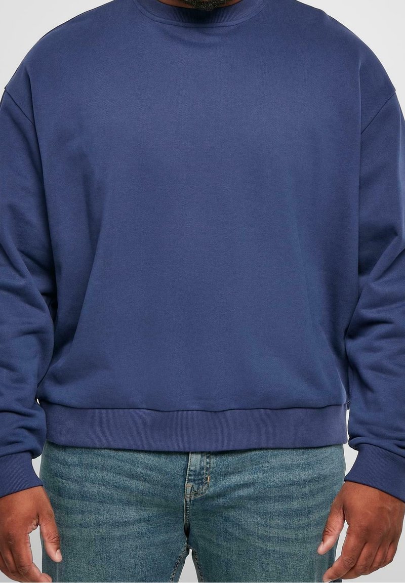 Sudadera de algodón azul marino con cuello redondo, con puños y dobladillo acanalados, en un corte relajado, combinada con jeans de color azul claro.