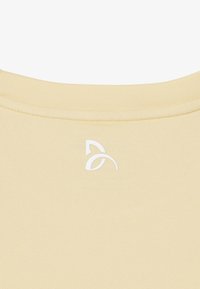 Gros plan sur l'encolure en tissu beige avec un petit logo abstrait blanc centré sous la couture du col.