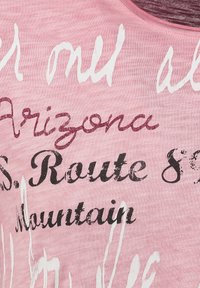 Camisa informal rosa hecha de una tela suave que presenta una mezcla de textos impresos en varias fuentes y colores: blanco, rojo intenso y negro.