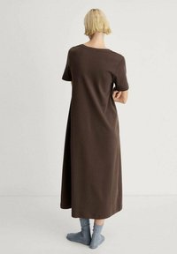 Vestito marrone fino al ginocchio, con maniche corte, dalla vestibilità rilassata e scollatura rotonda, abbinato a calzini alla caviglia leggeri di colore azzurro a coste.