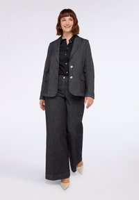 Tummaa harmaa bleiseri ja leveälahkeiset housut, joissa on halkiollinen kaulus, kaksi koristepainiketta ja sileä pinta. Musta paita alla.