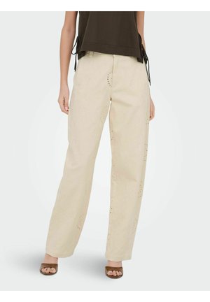 Personne portant un pantalon beige à jambes larges avec des motifs brodés subtils et des talons ouverts marron, assorti à un haut sans manches foncé.