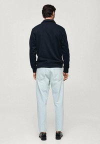 Marinblå tröja med krage, matchad med ljusblå, smalare jeans. Modellen har svarta skor; designen är enkel och utan dekoration.