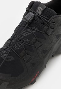 Schwarzer Trailrunning-Schuh mit strukturiertem Obermaterial, elastischem Schnürsystem und Contagrip-Laufsohle mit spitzen Traktionsstollen.