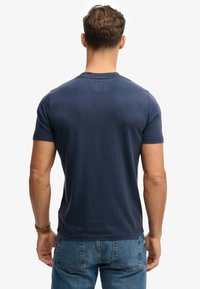 Camiseta de manga corta en azul marino, confeccionada en suave algodón, con un sencillo cuello redondo y un pequeño detalle de parche en la parte trasera.