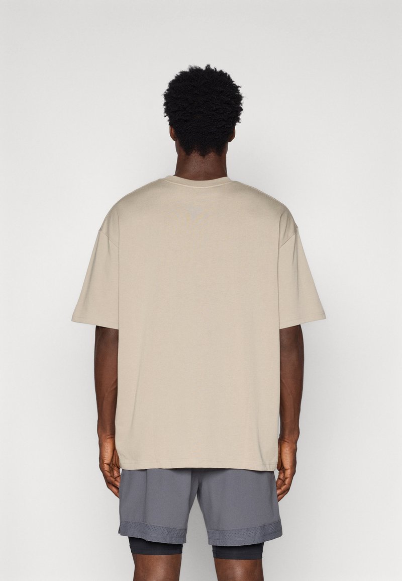 Maglietta in cotone beige con una vestibilità ampia e maniche corte, abbinata a pantaloni corti sportivi grigi. Superficie testurizzata, design semplice, retro non dettagliato.
