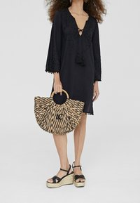 Svart klänning med broderade detaljer och trumpetärmar. Vävd halmhandväska med ett cirkulärt handtag och svart accent. Svarta kilklackar.