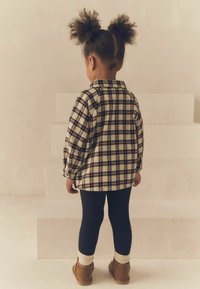 Kreminės, mėlynos ir rusvos spalvų languota flanelinė marškinė su ilgomis rankovėmis, derinama su juodomis tamprėmis ir rusvais batais. Matomos storos baltos kulkšninių kojinės.