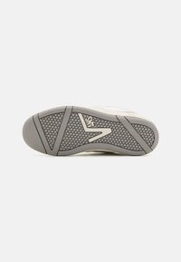 Biała podeszwa sneakersów z teksturowanym szarym gumowym wzorem, z wyraźnie wytłoczonym logo oraz kątowymi elementami designu zapewniającymi przyczepność.