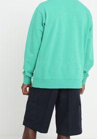 Felpa turchese con vestibilità ampia, polsini a costine, abbinata a pantaloni cargo blu navy con grandi tasche laterali e taglio morbido.