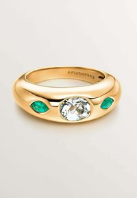 Anillo de banda de oro con una gran piedra clara en el centro, flanqueada por dos piedras verdes. Acabado liso y diseño redondeado.