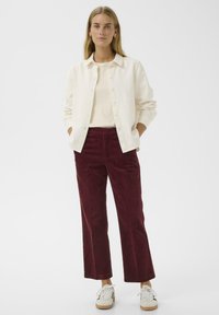 Krémová košile na knoflíky z slonoviny, krémový top pod ní, burgundské kordové kalhoty a bílé tenisky. Neformální outfit s volným střihem a texturovanou tkaninou.