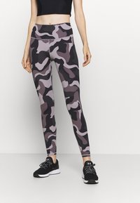 Kamouflageleggings i nyanser av grått och svart, med hög midja, stretchigt tyg och en slimmad design. Kombineras med svarta träningsskor.