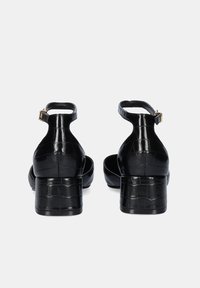 Sandalias de tacón negro con un patrón de cocodrilo brillante, correa ajustable en el tobillo y un tacón grueso. Presenta una textura suave y un hardware minimalista.