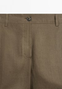 Front view of brown pants with a button closure and belt loops, showing fabric texture and stitching details.