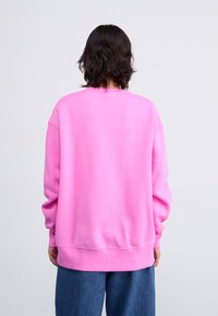 Sweatshirt rose surdimensionné avec un col rond et des poignets côtelés, fabriqué en tissu doux en mélange de coton. Vue de l'arrière.