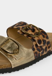 Ανοιχτό πέδιλο με διπλούς φαρδιούς λουριά, ένα μεταλλικό χρυσό, ένα με λεοπάρ μοτίβο, το καθένα με μεγάλο χρυσό πόμολο και μαύρη ραβδωτή σόλα.