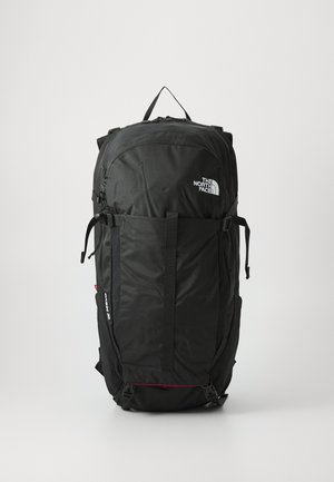 Mochila negra con un tejido texturizado y duradero. Cuenta con correas ajustables, un asa en la parte superior y un bolsillo frontal con cremallera. Logotipo exhibido de forma prominente.