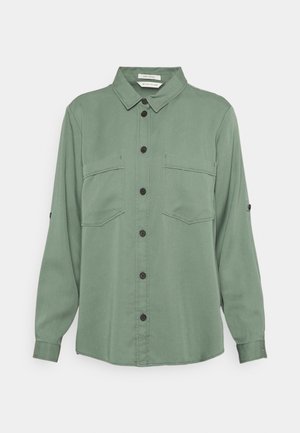 Camicia verde a maniche lunghe con bottoni, due tasche sul petto e colletto, mostrata su uno sfondo semplice.