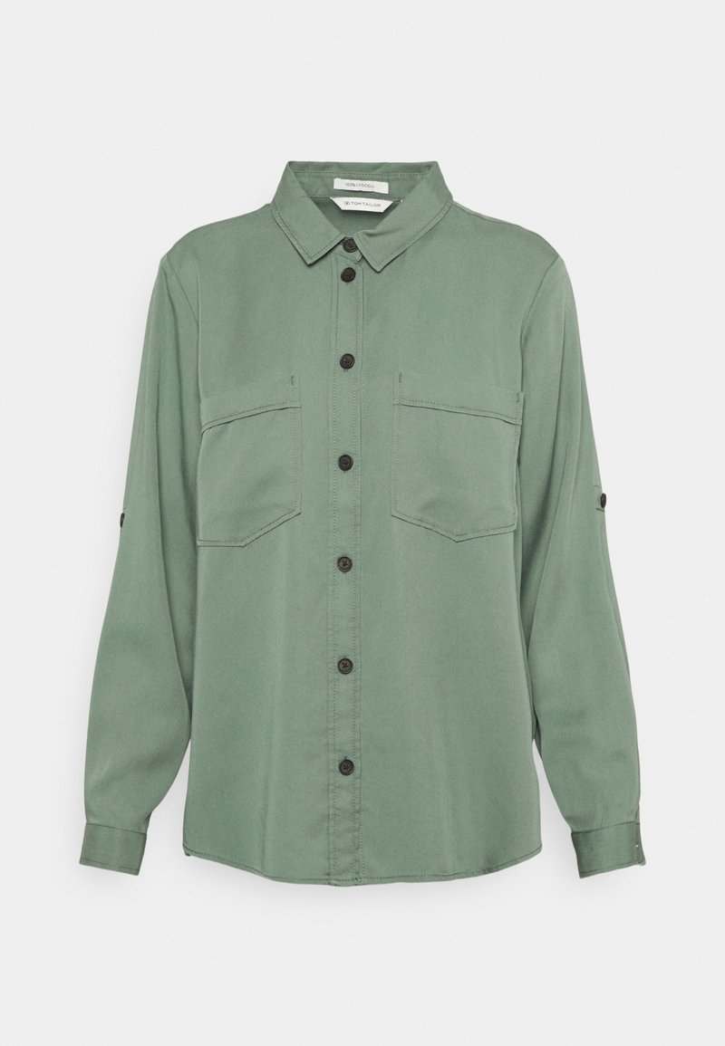 Chemise verte à manches longues avec boutons, deux poches poitrine et col, présentée sur un fond uni.