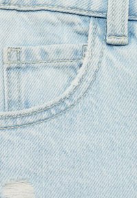 Svetrna svetlo modra denim tkanina z zbledelim teksturo, ki vključuje obližno žeper in vidne šive. Prisotni so rahlo strgani robovi.
