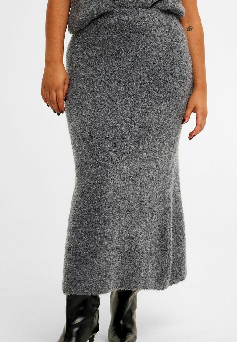 Gray wool blend maxi skirt with a soft texture, fitted at the waist, flaring slightly towards the hem, paired with black knee-high boots.