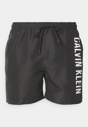 Crne kupaćice od glatkog materijala, s elastičnim pojasom koji se može zategnuti i bijelim natpisom "CALVIN KLEIN" sa strane.
