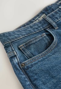 Sinised teksad klassikalise viie tasku disainiga, kontrastse õmblusega ja väikese metallnupuga esimeses taskus.