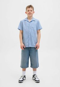 Modra in bela črtasta majica s kratkimi rokavi in �žepom, v kombinaciji z denim kratkimi hlačami do kolen ter črno-belimi športnimi copati.