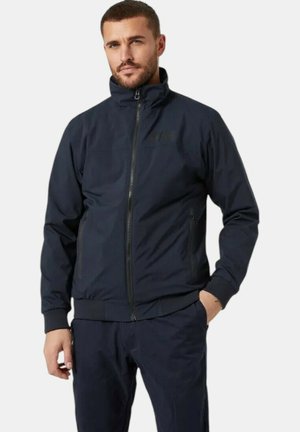 Chaqueta azul marino con cuello alto, cremallera frontal y puños elásticos. Cuenta con bolsillos laterales y una tela suave y ligera.
