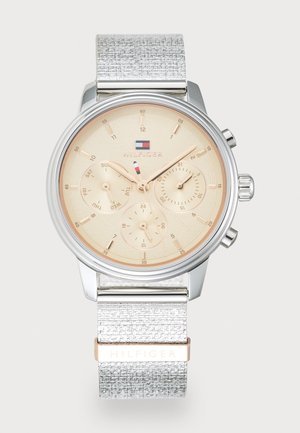 Montre-bracelet en métal argenté avec un cadran doré clair, trois sous-cadrans et un bracelet argenté texturé présentant un accent doré avec le nom de la marque.